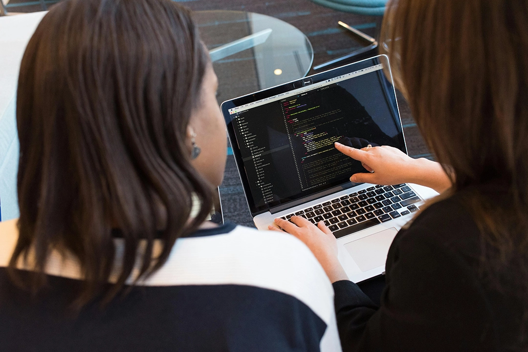 Two Women working together on a laptop with code on the screen.